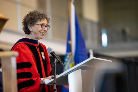 A woman wearing academic regalia speaks at a podium. 