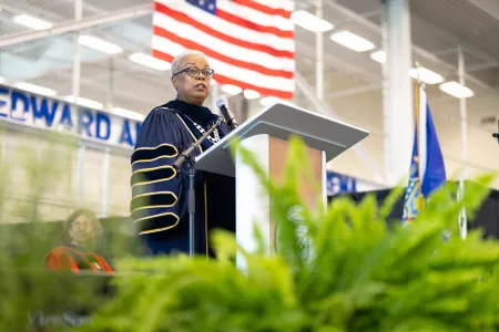 A woman in academic regalia speaks at a podium. 