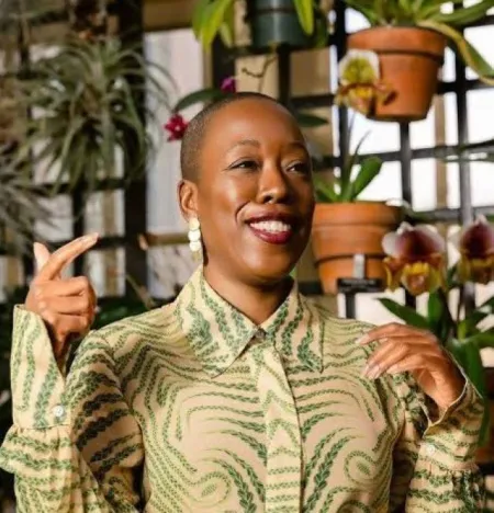 Headshot of Jefreen M. Hayes. Jefreen is wearing a beige and green pattern button down shirt and is posed in front of potted plants.