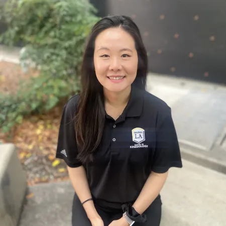 Headshot of Saemi Lee. Saemi is posed in front of small green foliage. She is wearing a black polo with white logo on left chest.