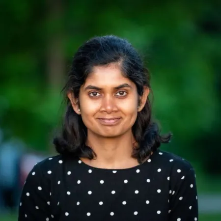 Headshot of Sayanti Mondal. Sayanti is wearing a black top with white polka dots. Is posed in front of blurred green background.