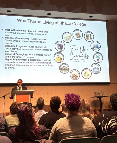 man standing at podium with text on screen behind him