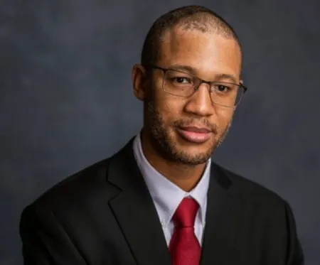 Headshot of Tyrell Stewart-Harris. Tyrell is wearing a black suit with a white dress shirt and red tie.