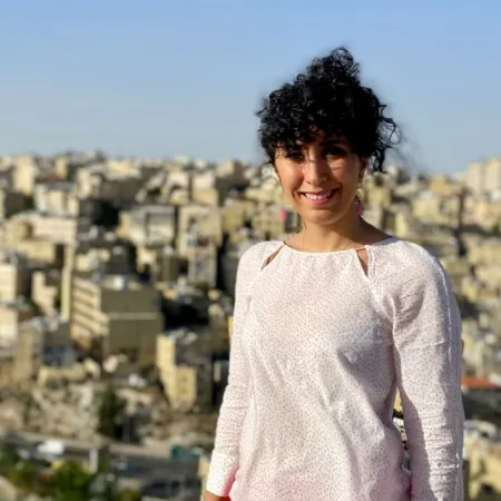 Image of Zohreh posed with a cityscape in the background. Zohreh is wearing a white long sleeve top.