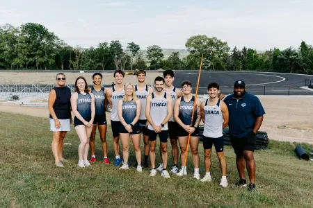 College students and coaches pose for a group photo by a track that is under construction.