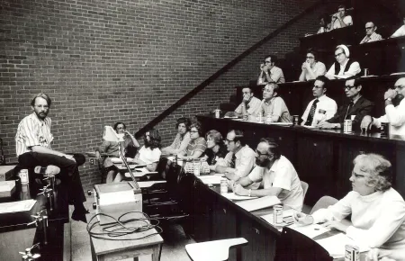 A black and white photo of a lecture hall with students and a professor.
