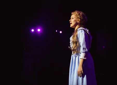 A college student sings onstage in a musical. 