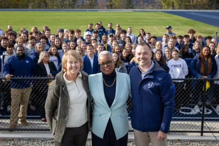 Three people pose and smile in front of a college track team.