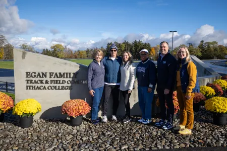 Six people pose in front of a sign that says "Egan Family Track & Field Complex, Ithaca College."