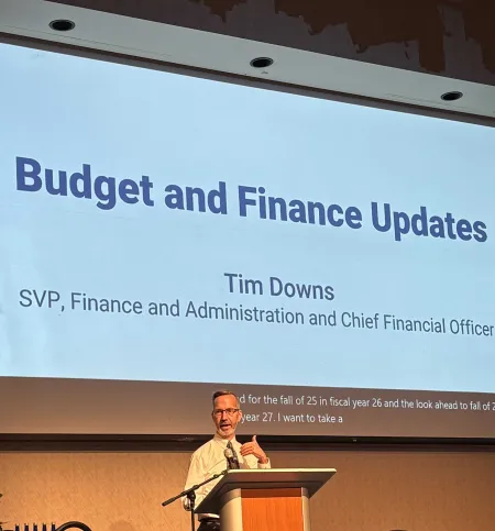 Man with beard stands at lectern with slide behind him.