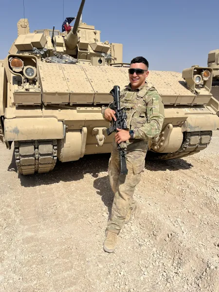A soldier stands in front of a tank in the desert.