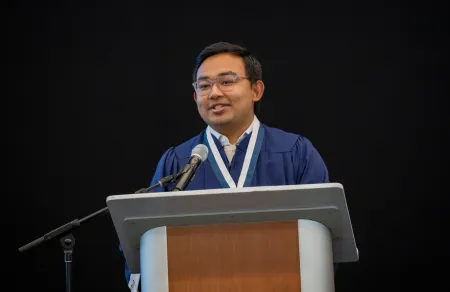 A student addresses fellow graduates at a podium.