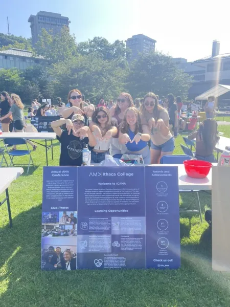 A group of students on campus with a poster conveying info about IC's AMA chapter.