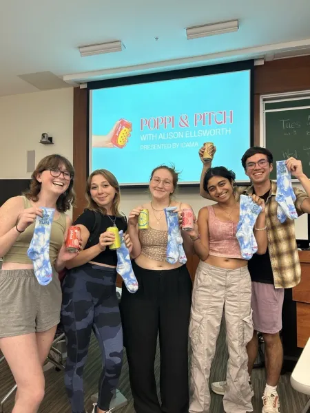 Students stand in front of a screen that says "Poppi & Pitch."