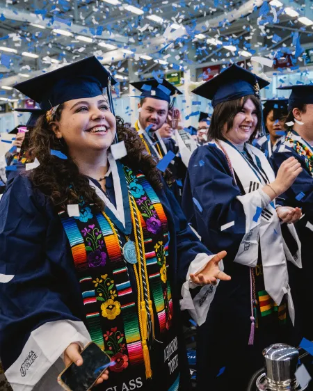 Graduates in caps and gowns smile as confetti falls.