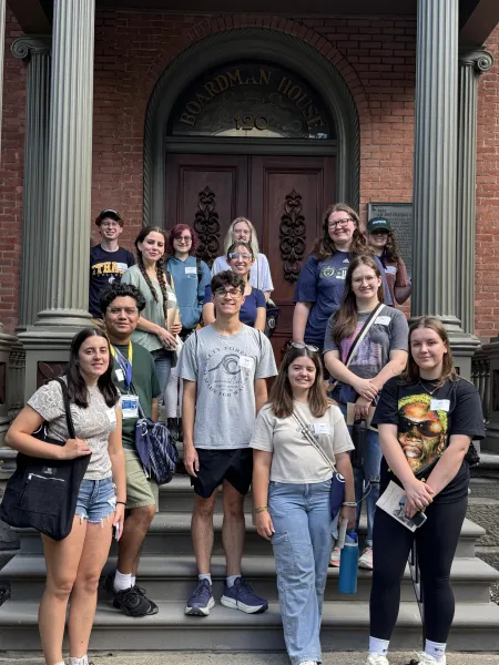 Group of students standing on the front steps of a historic brick home
