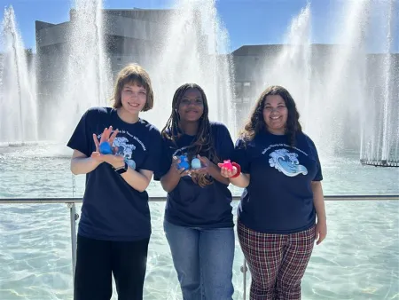 Students holding whales in front of fountain 