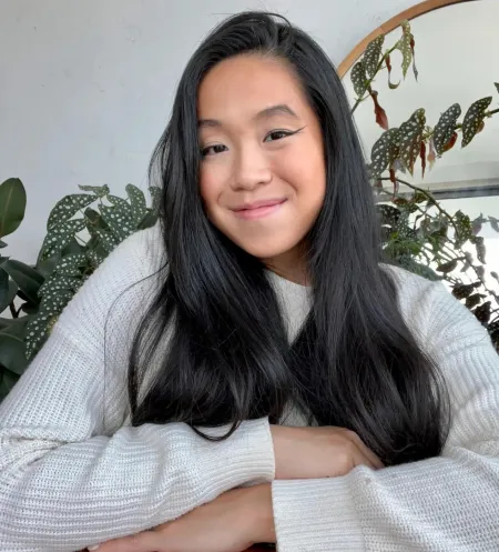 Woman with long dark hair in front of a plant