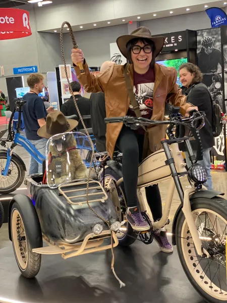 A woman dressed as Indiana Jones sits on a motorcycle.