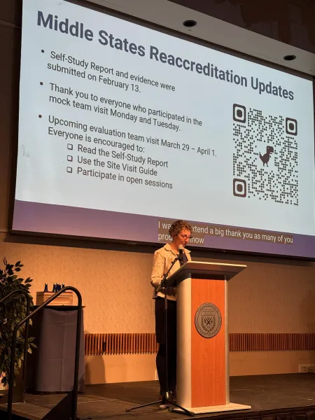 woman in a white top standing at a lectern with a slide projected behind her