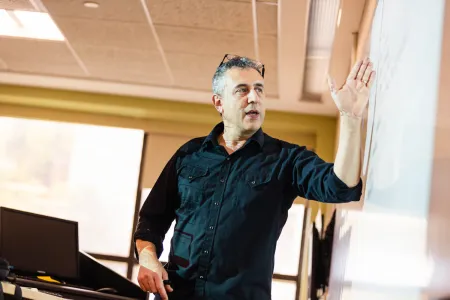 Man wearing a dark shirt standing at a whiteboard.