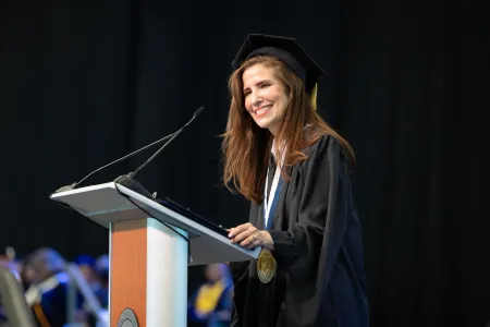 A woman at a podium in cap and gown.