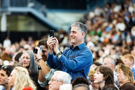 A man with a phone records Commencement from the stands.