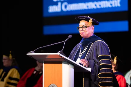 A woman wearing a cap and gown addresses the audience.