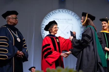 Women wearing caps and gowns congratulate graduates.