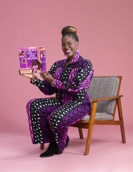 An author, wearing purple, sits in a chair and displays her book.