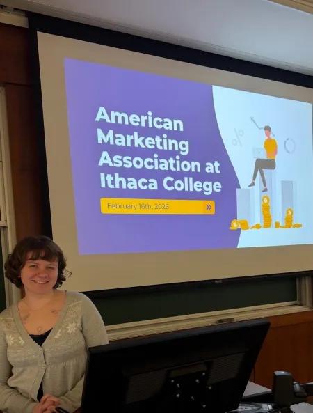 A student is standing in front of a powerpoint screen that reads American Marketing Association at IC.