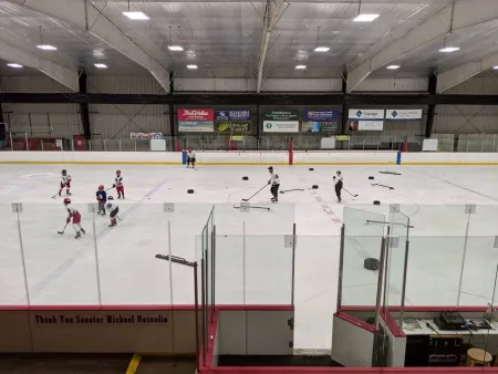 Indoor ice rink with skaters dressed in hockey gear practicing on the ice.