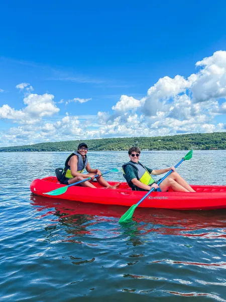 Two college students pilot a red kayak.