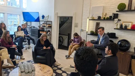 A faculty member is speaking with a group of students seated around him in comfortable chairs.