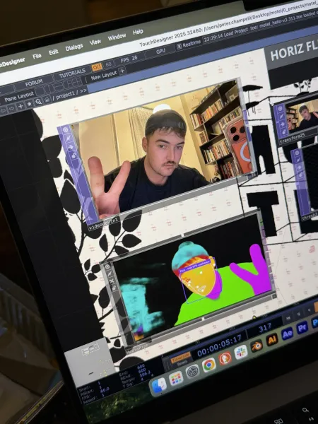 A laptop screen shows Peter Champelli’s webcam feed in TouchDesigner, next to a MediaPipe view that maps his face, body, and hand in bright colors.