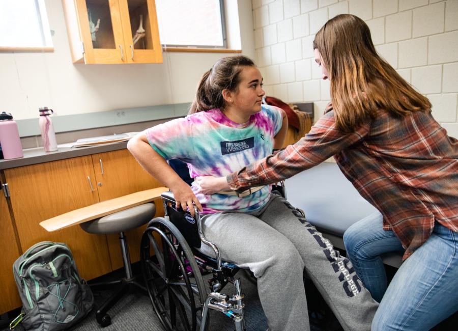 Two students are practicing transfers from a wheelchair.