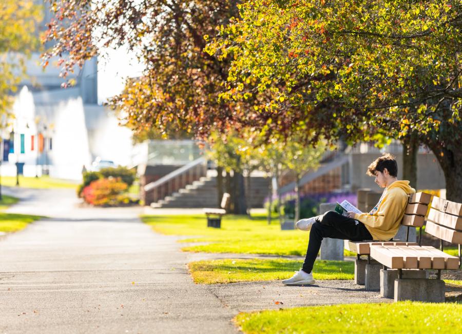 A picture of a student sitting on a bench near the fountains at Ithaca College.