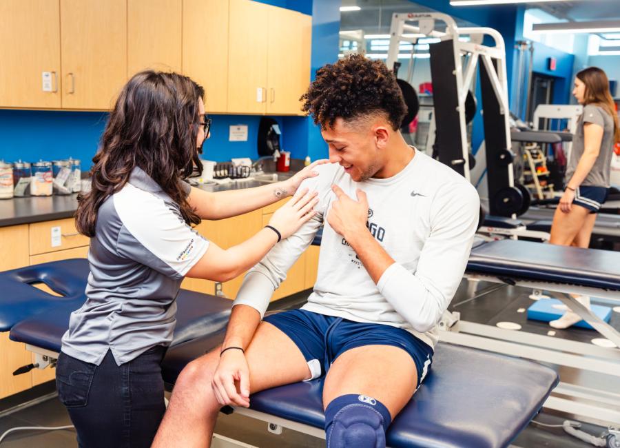 a female student examines the shoulder of a male student dressed in athletic attire