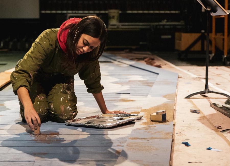 Ithaca College student on hands and knees painting a mural