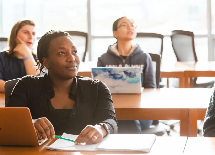 Three students are seated listening to a faculty member lecture.