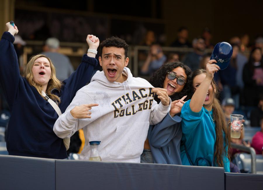 Image of Fans at Cortaca 2022. Fan is pointing to a hoodie with Ithaca College embroidered across chest. Other fans celebrating around him.