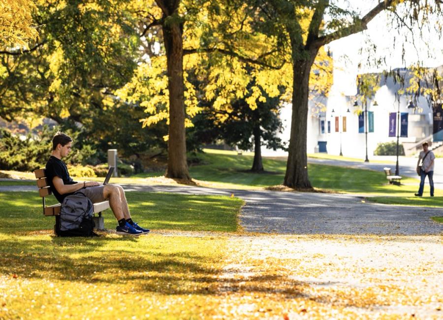 Student sitting on a bench along the academic quads of Ithaca College, with the Fountains in the background.