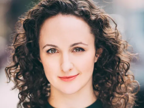 Headshot of playwright Kate Hamill, a white-skinned woman with curly brunette hair.