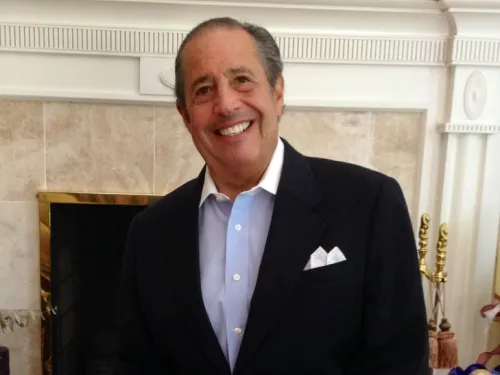 An older gentleman poses for a photo in a suit, button-down shirt, and slacks. 