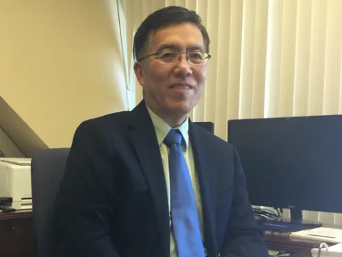 A man in glasses, a dark suit, and blue tie. 