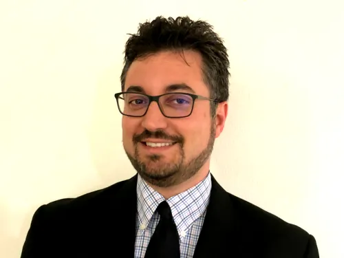 A bearded man wearing glasses and a business suit