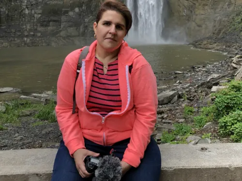A woman with a camera sitting in front of a waterfall
