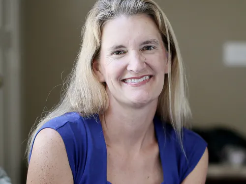 A caucasian, blonde woman sits and smiles at the camera. 