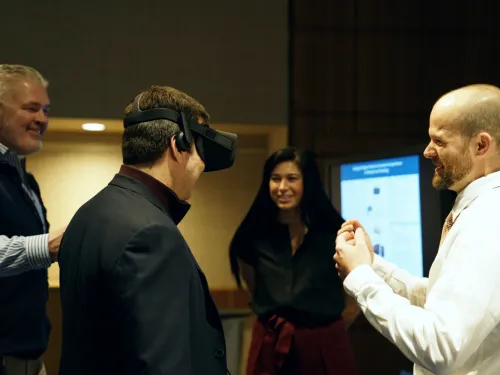 A man wearing VR goggle stands with three other people