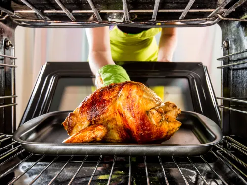 A person taking a chicken from an oven
